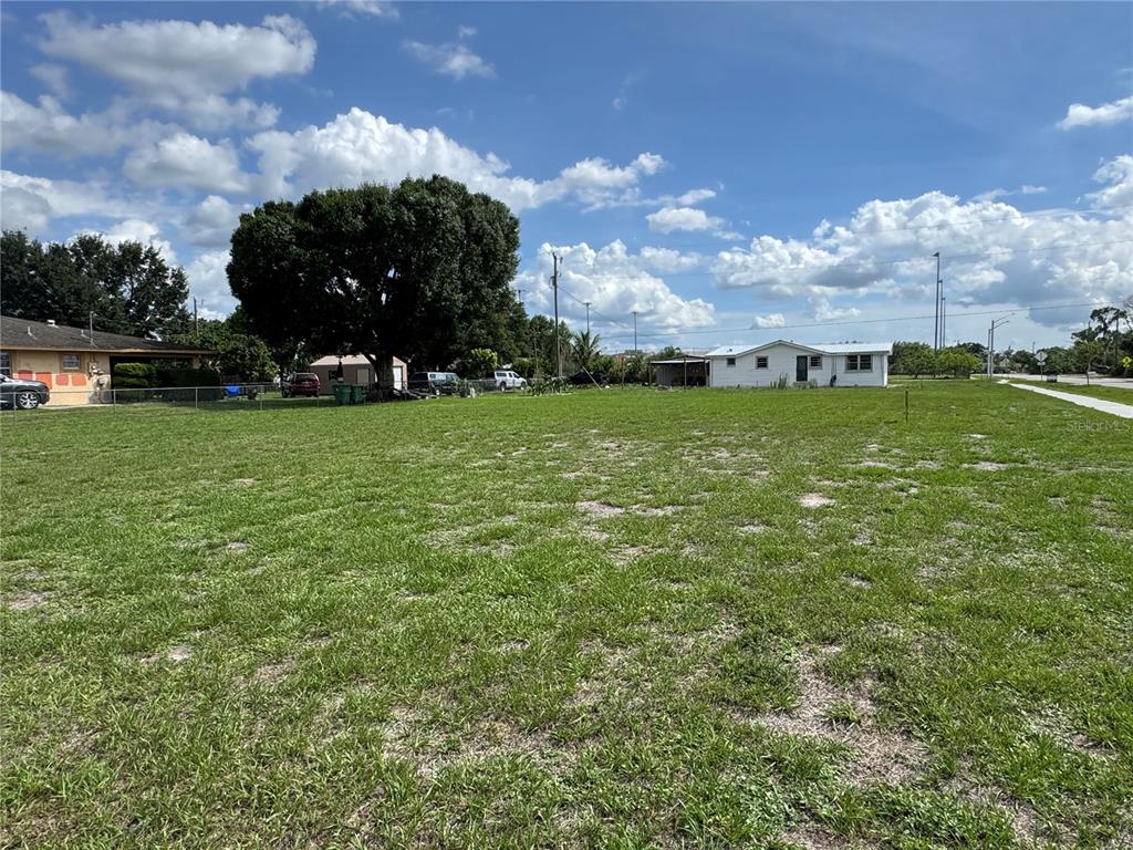 A large, grassy vacant lot with a few surrounding houses and trees under a cloudy sky — GLADES AVENUE, IMMOKALEE, FL