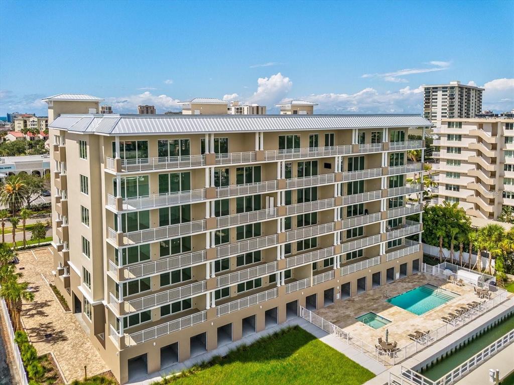 An exterior view of a multi-story apartment building with balconies, a swimming pool, and landscaping — 125 ISLAND WAY UNIT 305, CLEARWATER, FL