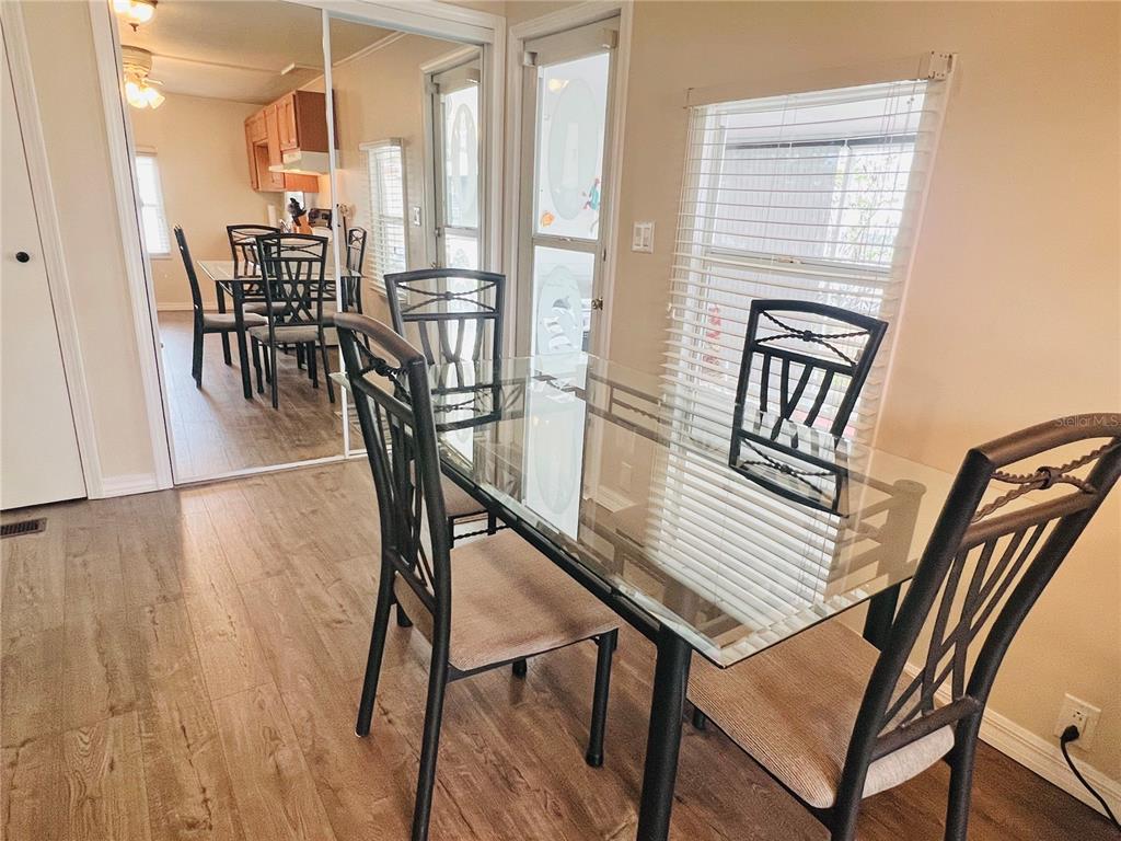 A dining area features a glass-topped table, metal chairs, wood-look flooring, and mirrored closet doors — 2282 PIAZZA DRIVE UNIT 117, SARASOTA, FL
