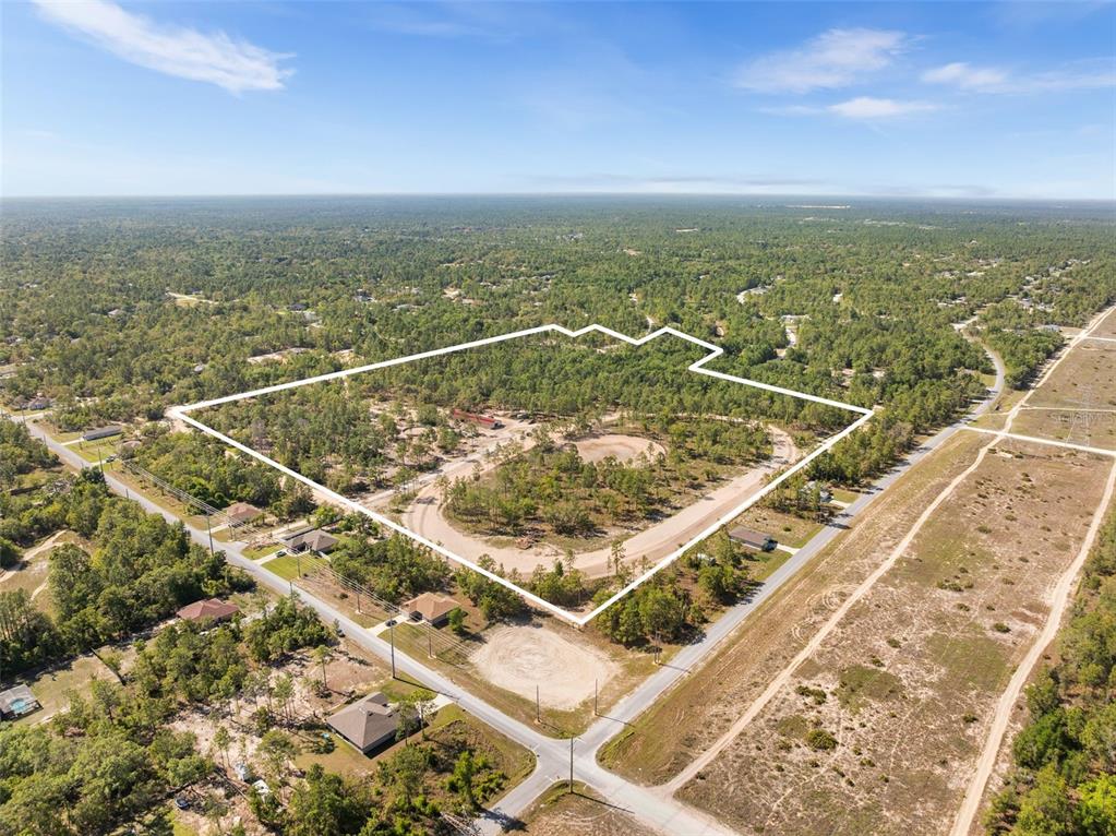 An aerial view shows a wooded residential area with dirt roads and scattered houses — 25723 BAREVA ROAD, WEEKI WACHEE, FL