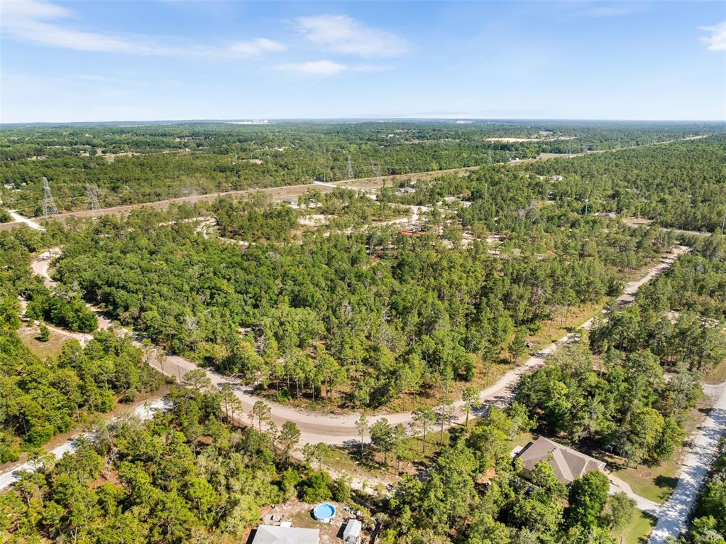 A long, light-colored horse barn with multiple stalls sits on a sandy, cleared lot — 25723 BAREVA ROAD, WEEKI WACHEE, FL