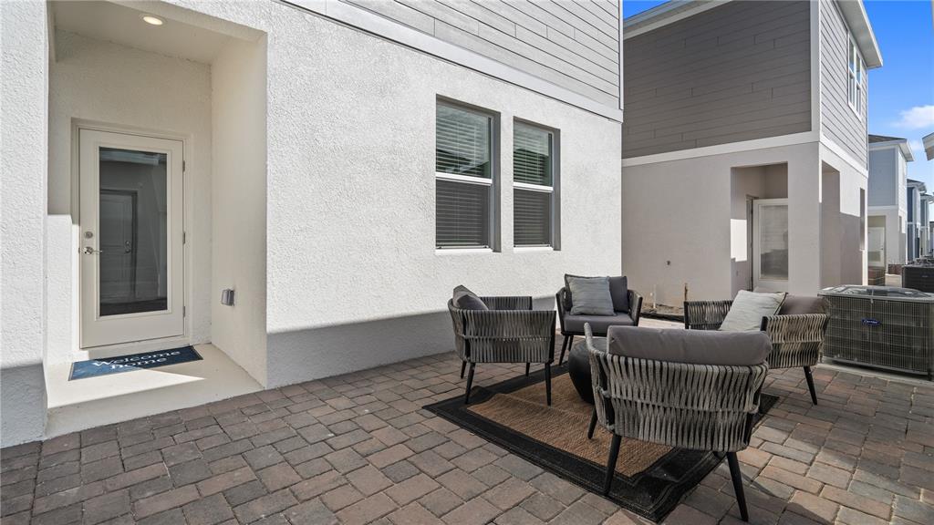 A paved patio features four gray wicker chairs arranged around a rug near a house — 1812 RIDER RAIN LANE, APOPKA, FL