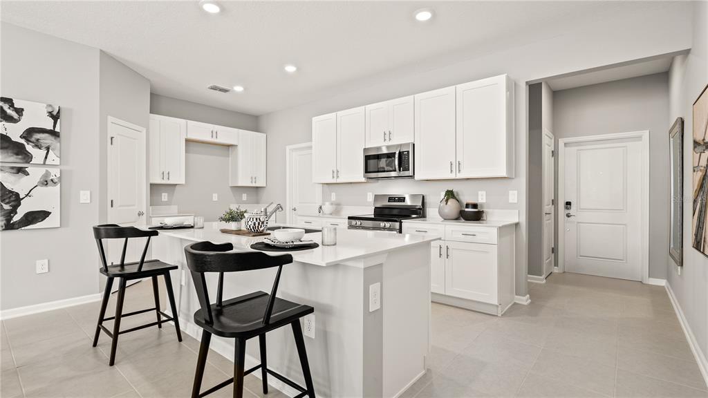 A modern kitchen features white cabinets, a central island with black stools, and tile flooring — 1812 RIDER RAIN LANE, APOPKA, FL