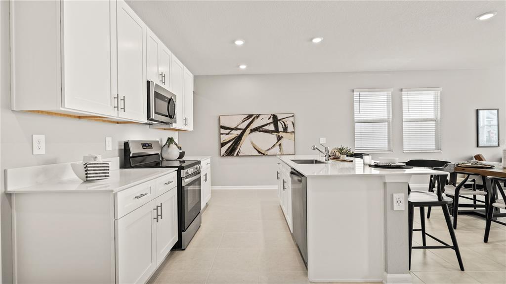 A modern kitchen features white cabinets, stainless steel appliances, and a large central island — 1812 RIDER RAIN LANE, APOPKA, FL