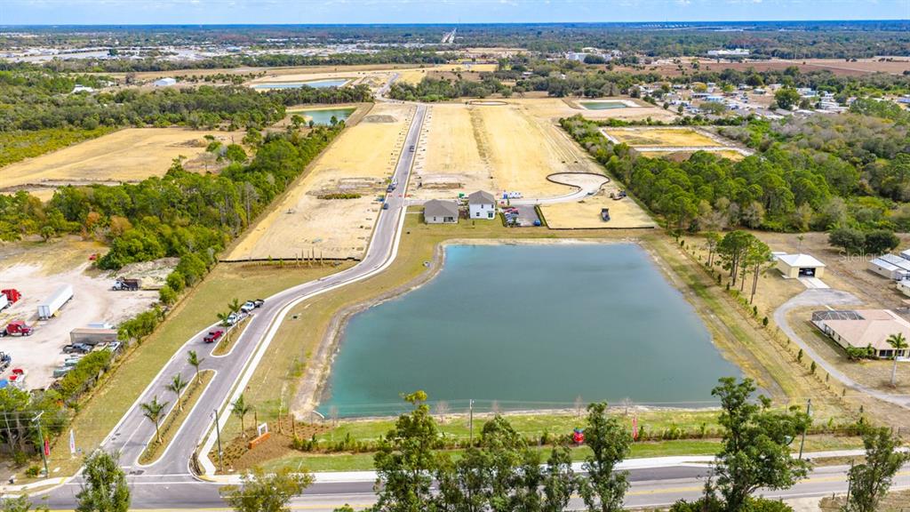 An aerial view shows a residential development site with a large pond and paved roads — 6778 EQUINOX LANE, NORTH FORT MYERS, FL