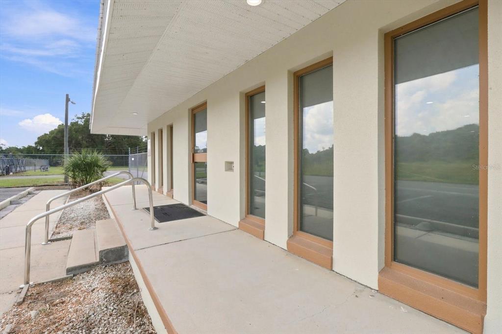An exterior view of a building entrance with a concrete walkway, metal railing, and windows — 50 DIANA STREET, INGLIS, FL