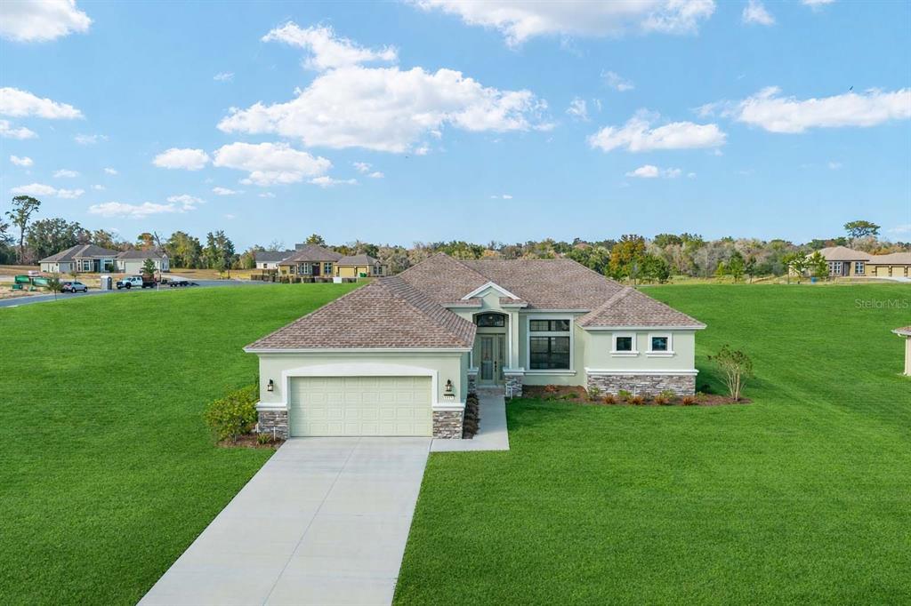 A single-story house with a two-car garage and stone accents sits on a large lawn — 1499 E PEGASUS LANE, INVERNESS, FL