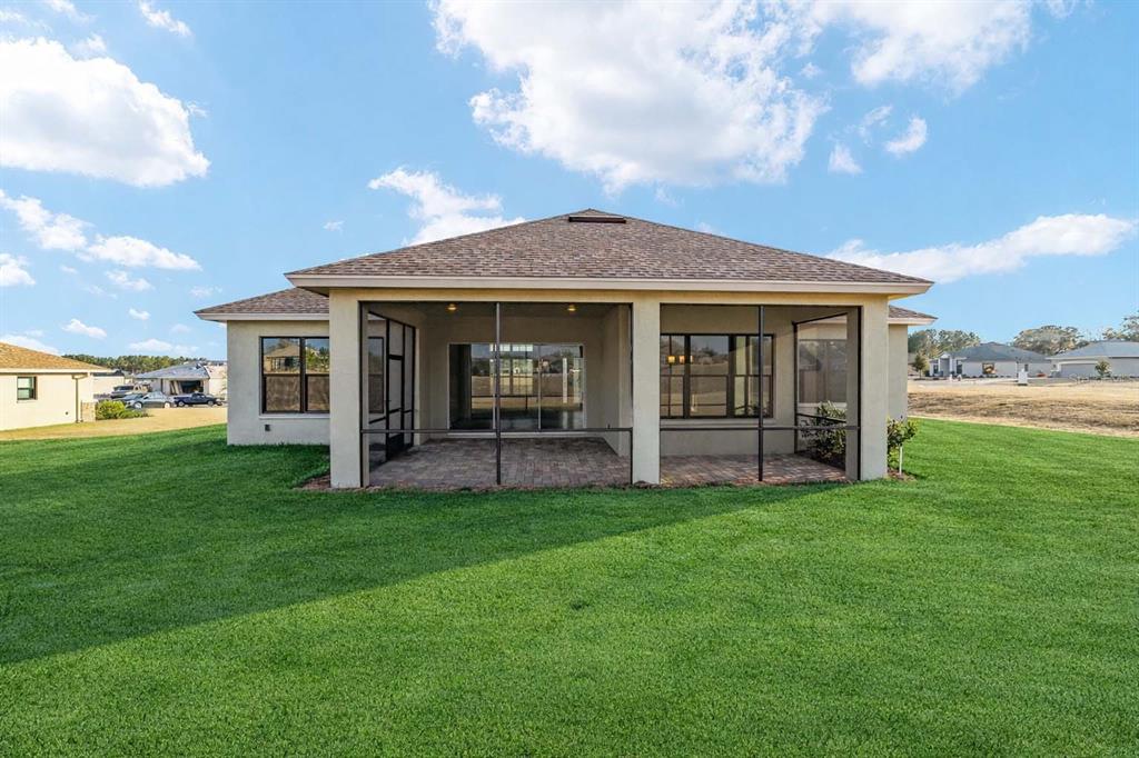 A rear view of a single-story house with a screened-in patio and a large lawn — 1499 E PEGASUS LANE, INVERNESS, FL