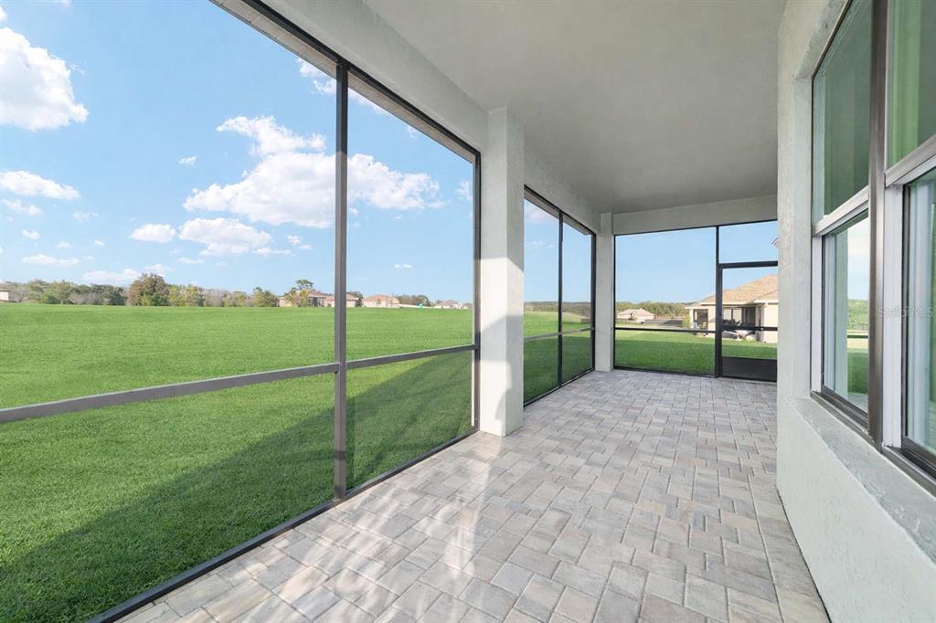 A screened-in patio with paver flooring overlooks a large, open grassy field — 1499 E PEGASUS LANE, INVERNESS, FL