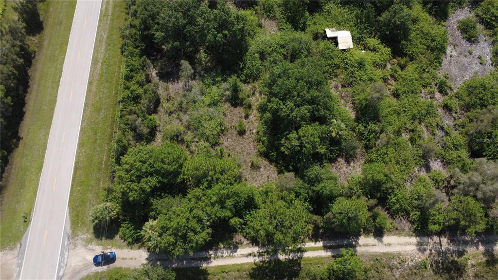 An aerial view shows a wooded lot with a small structure next to a road — 30391 OIL WELL ROAD, PUNTA GORDA, FL