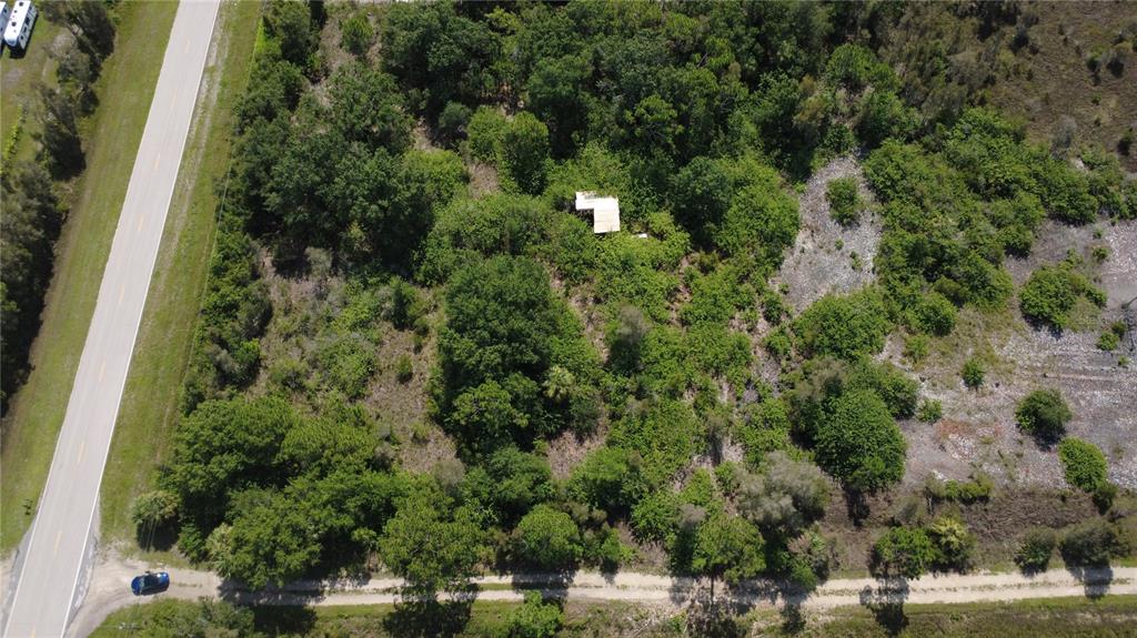 An aerial view shows a small, light-colored structure nestled within a wooded, undeveloped lot — 30391 OIL WELL ROAD, PUNTA GORDA, FL