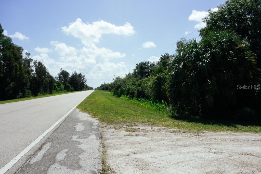 A paved road stretches into the distance beside a grassy shoulder and dense trees — 30391 OIL WELL ROAD, PUNTA GORDA, FL
