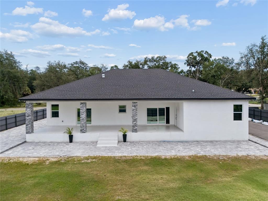 A white house with a dark shingled roof, stone-accented columns, and a paved patio area — 3944 WHITE HERON DRIVE, ORLANDO, FL