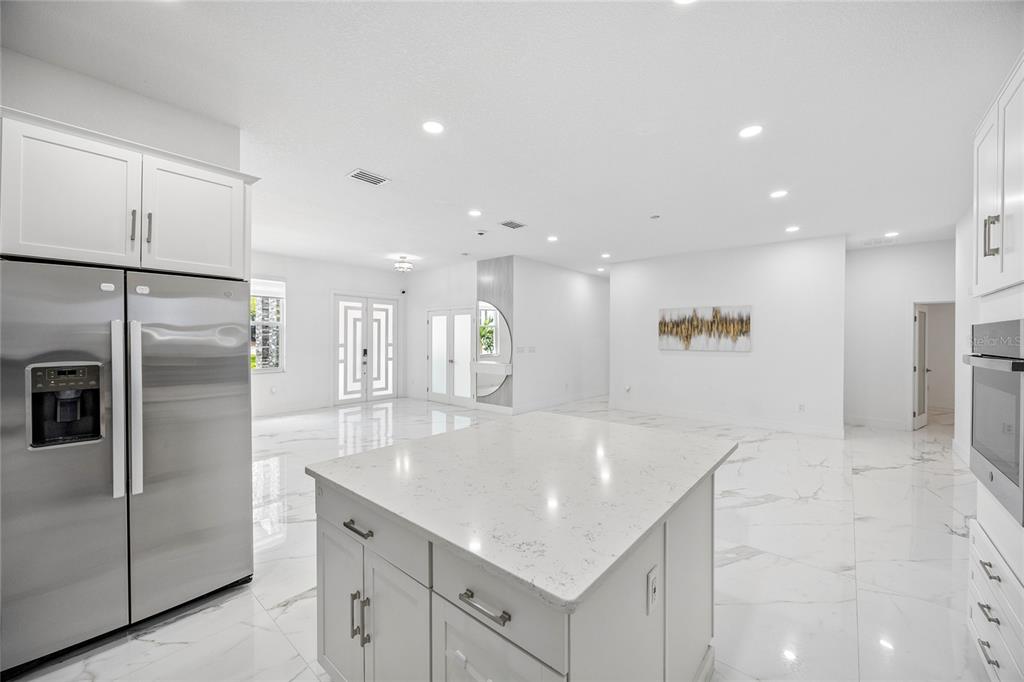 A modern kitchen with a white quartz island, stainless steel refrigerator, and white marble flooring — 3944 WHITE HERON DRIVE, ORLANDO, FL
