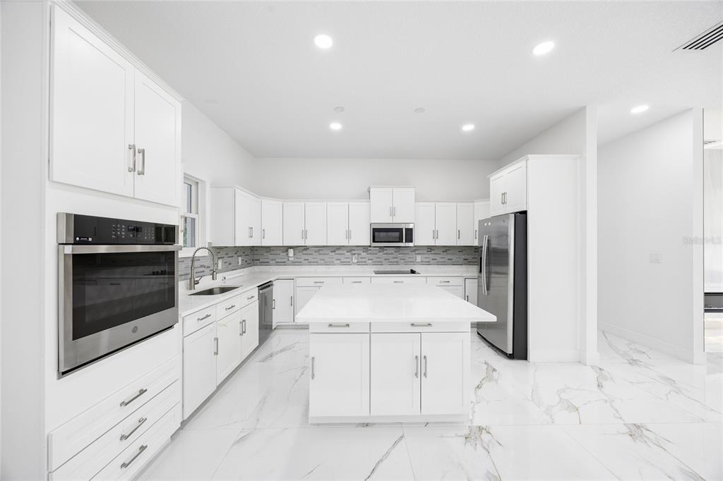 A modern white kitchen featuring an island, stainless steel appliances, and marble-look tile flooring — 3944 WHITE HERON DRIVE, ORLANDO, FL