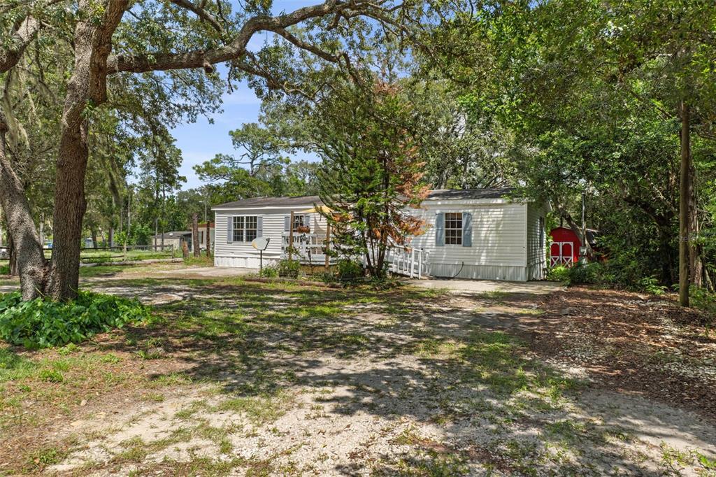 A single-story mobile home with white siding sits on a wooded lot with a driveway — 3322 SUSAN DRIVE, SPRING HILL, FL