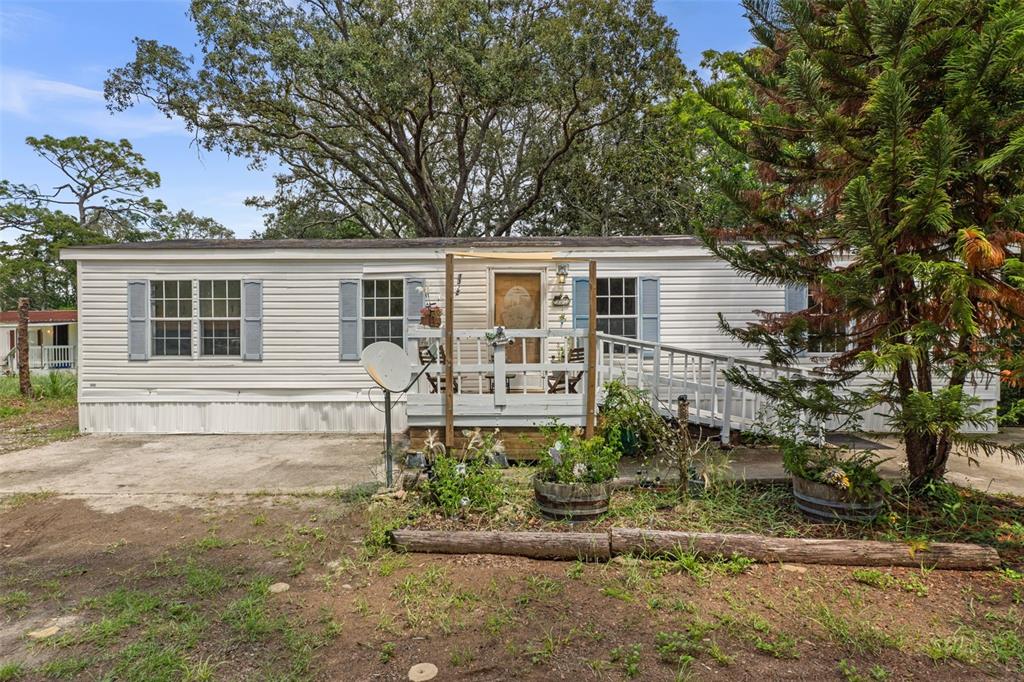 A white mobile home features a wooden front deck with a ramp and blue shutters — 3322 SUSAN DRIVE, SPRING HILL, FL