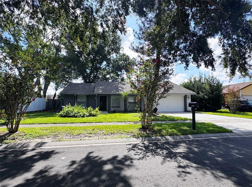 A single-story house with a white garage, gray siding, and a green lawn under trees — 12225 PANTAR STREET, ORLANDO, FL
