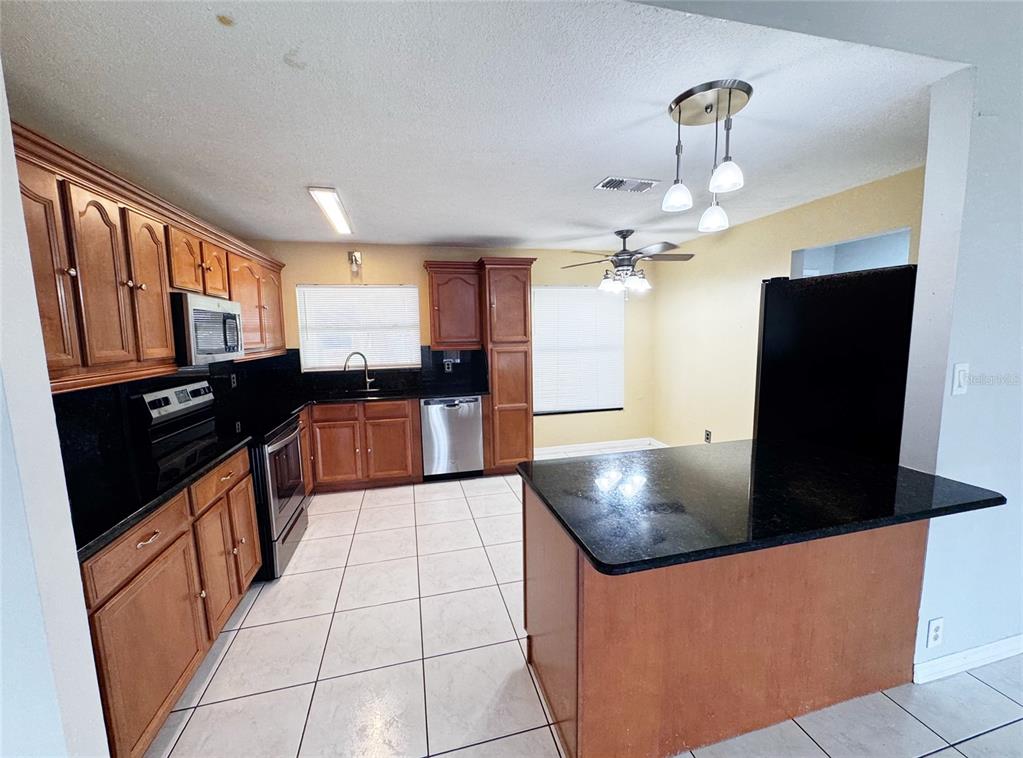 A spacious room with white tile flooring, a ceiling fan, and an open kitchen area — 12225 PANTAR STREET, ORLANDO, FL