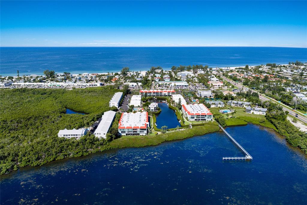 An aerial view shows a coastal condominium complex surrounded by mangroves and a large bay — 3705 E BAY DRIVE UNIT 115, HOLMES BEACH, FL