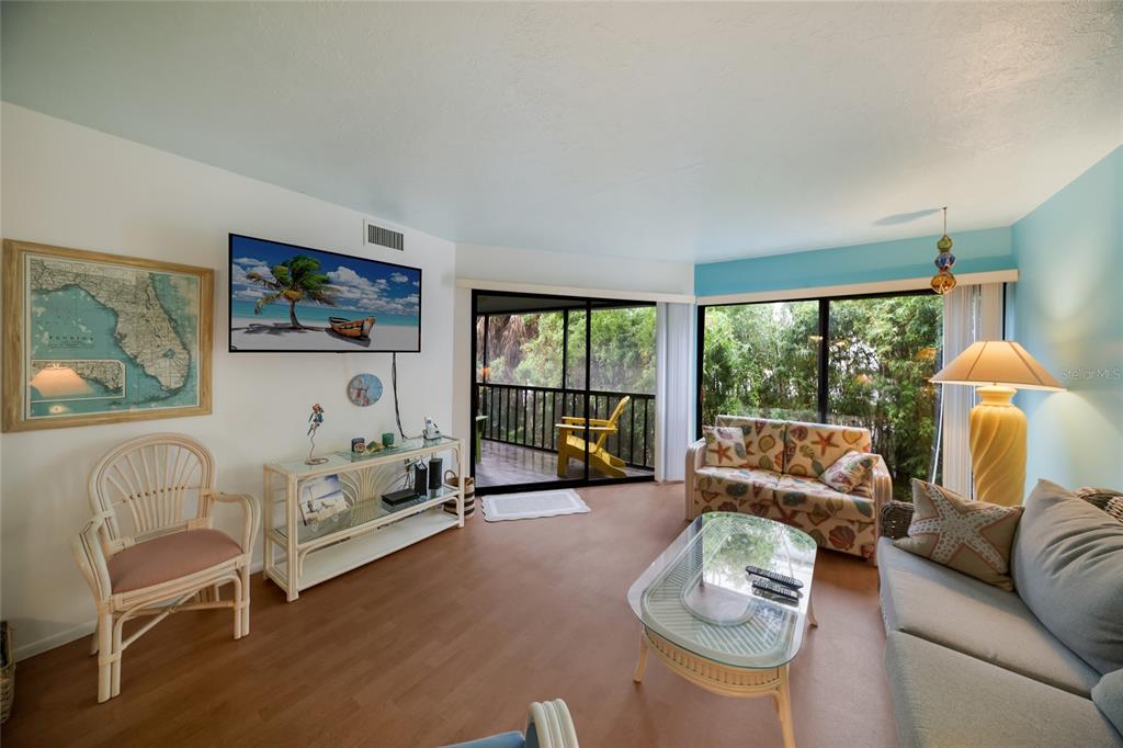 A living room features a television, a glass coffee table, and a view of a balcony — 3705 E BAY DRIVE UNIT 115, HOLMES BEACH, FL