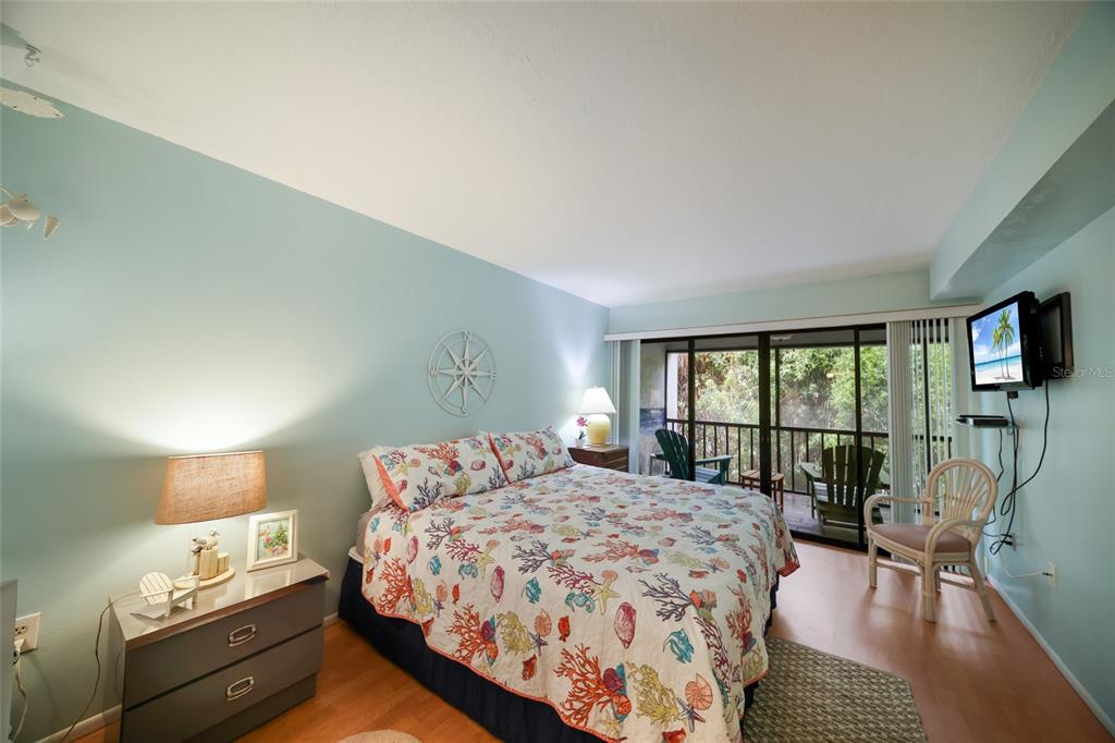 A bedroom features a coral-patterned bedspread, light blue walls, and a sliding door to a balcony — 3705 E BAY DRIVE UNIT 115, HOLMES BEACH, FL