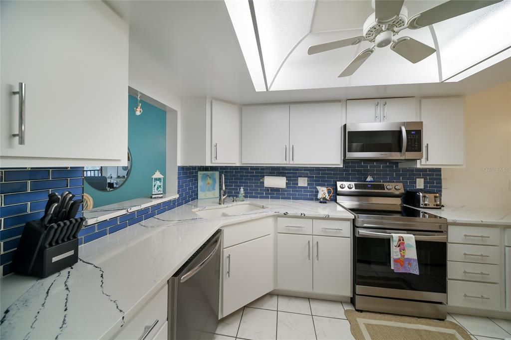 A kitchen features white cabinets, blue subway tile backsplash, stainless steel appliances, and quartz countertops — 3705 E BAY DRIVE UNIT 115, HOLMES BEACH, FL