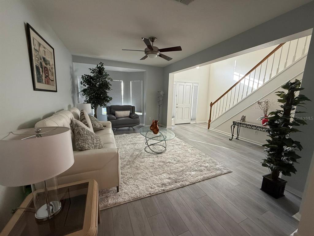 A living room features light wood-look flooring, a white sofa, and a staircase — 424 FLATWOOD DRIVE, WINTER SPRINGS, FL