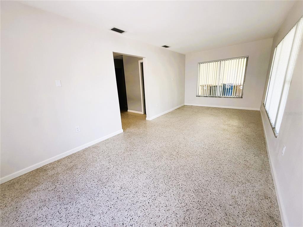 A living room with light walls, vertical blinds, and speckled flooring — 14017 W PARSLEY DRIVE, MADEIRA BEACH, FL