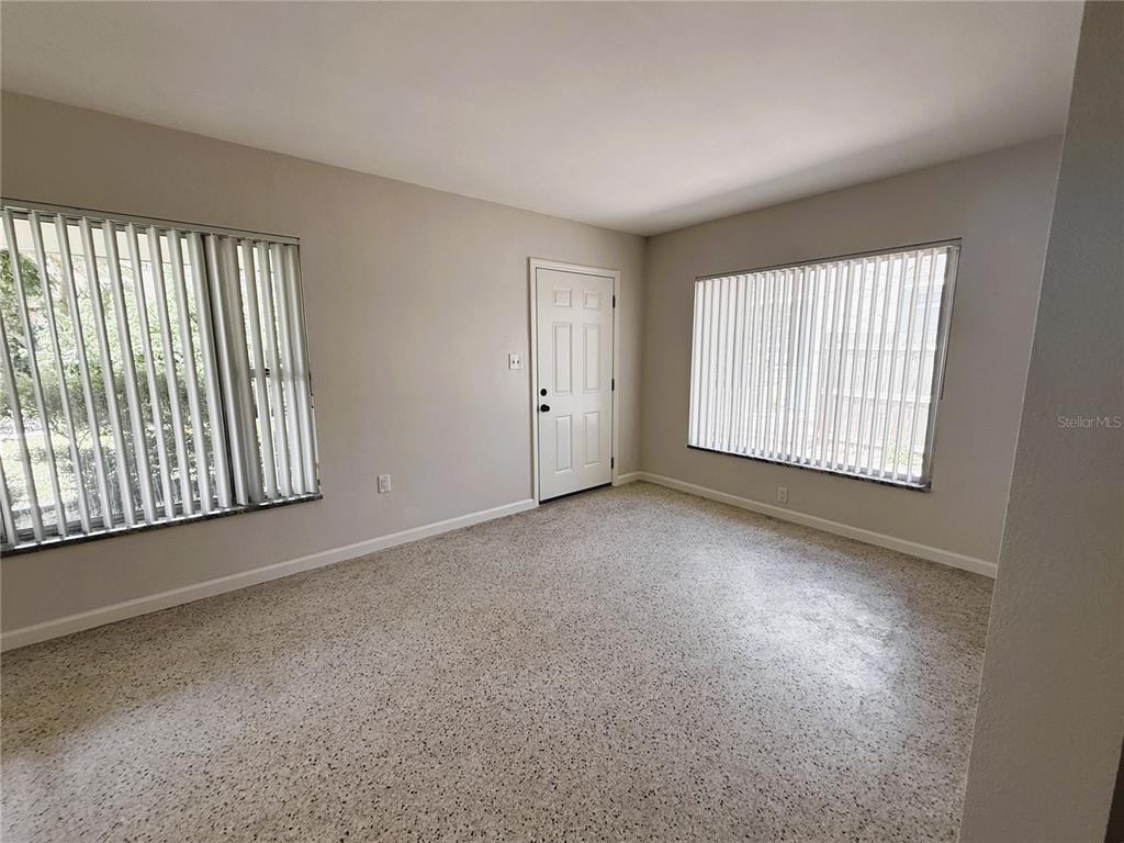 A living room features light-colored walls, terrazzo flooring, vertical blinds, and a white front door — 14017 W PARSLEY DRIVE, MADEIRA BEACH, FL