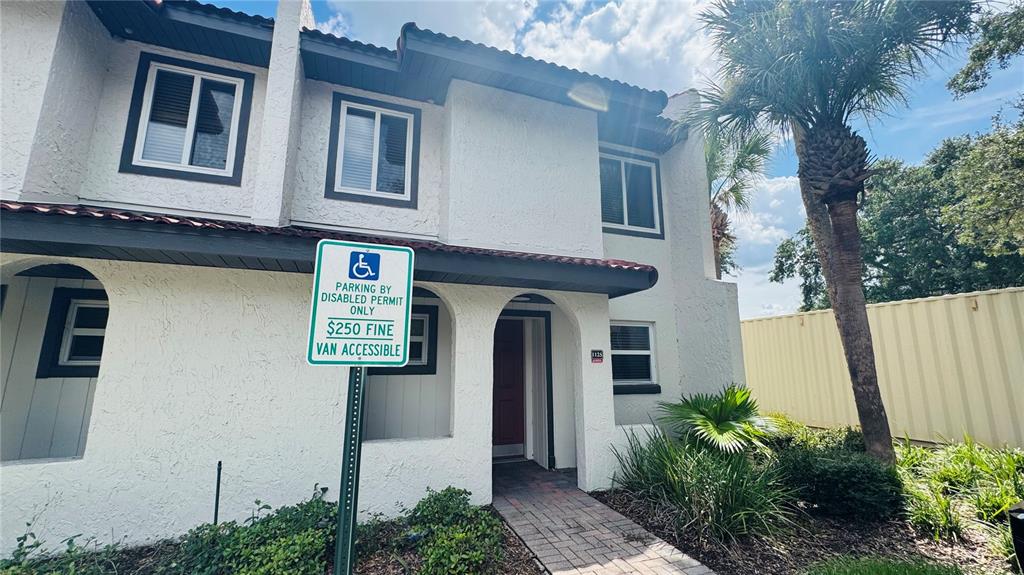 A two-story white stucco townhouse features a red door and a handicap parking sign — 1125 SPACEPORT COURT, KISSIMMEE, FL