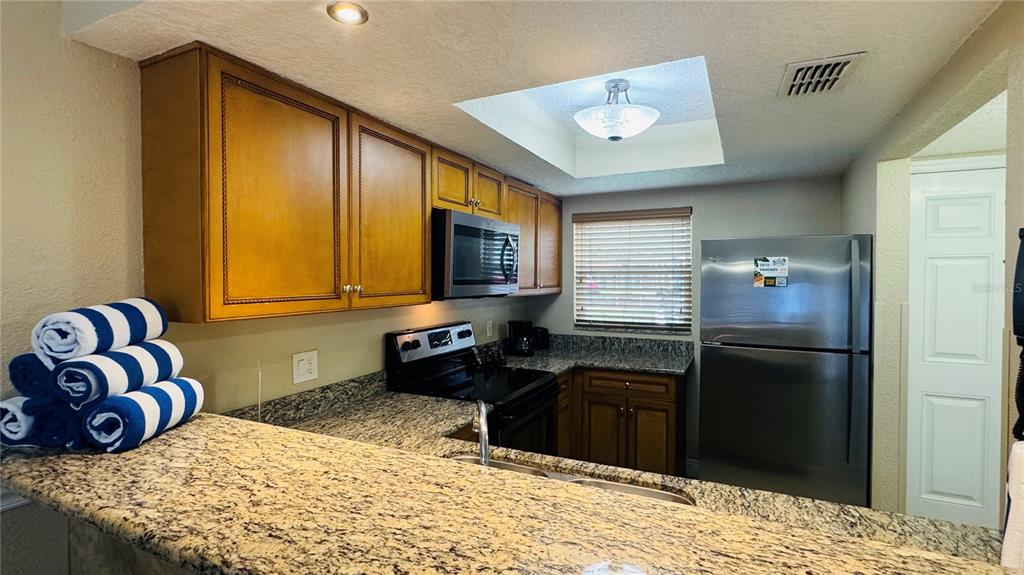 A kitchen features wood cabinets, granite countertops, stainless steel appliances, and a skylight — 1125 SPACEPORT COURT, KISSIMMEE, FL