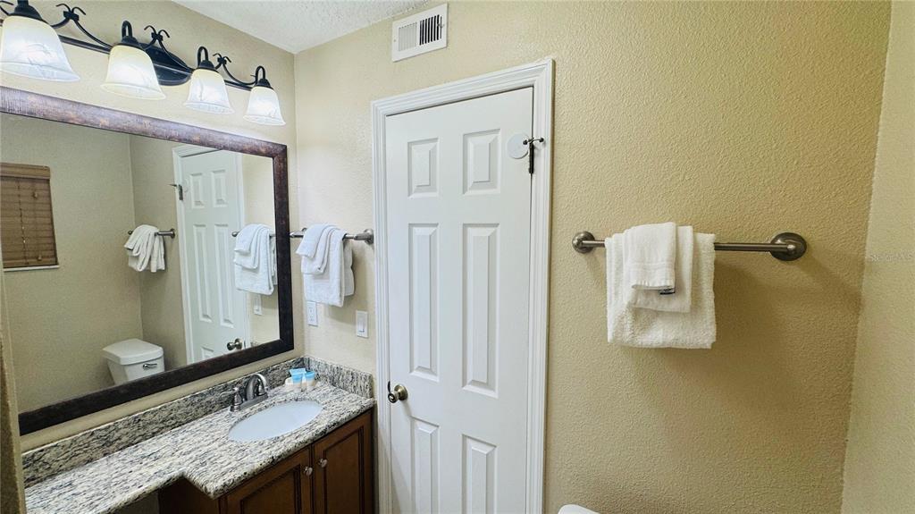 A bathroom features a granite vanity, a framed mirror, and a white door — 1125 SPACEPORT COURT, KISSIMMEE, FL