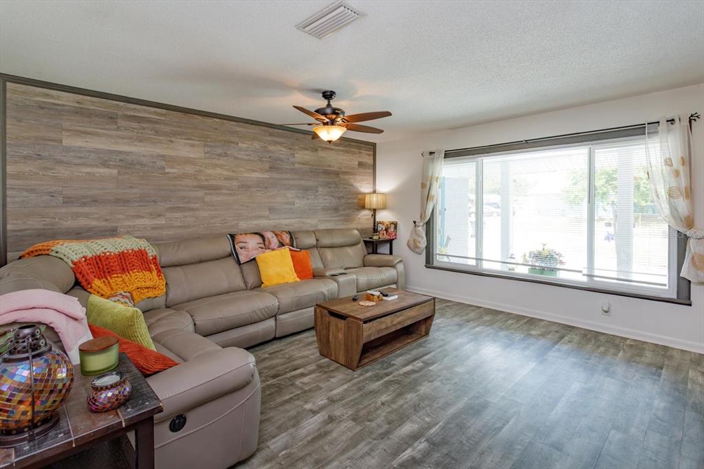 A living room features a wood-paneled accent wall, a large sectional sofa, and wood-look flooring — 5325 SHARLENE DR, TITUSVILLE, FL