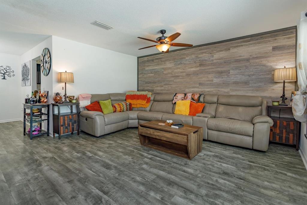 A living room features a large sectional sofa, a wood-paneled accent wall, and wood-look flooring — 5325 SHARLENE DR, TITUSVILLE, FL