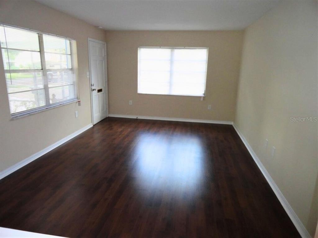 An empty room features dark wood-look flooring, beige walls, and two windows with blinds — 610 S LAKE FORMOSA DRIVE, ORLANDO, FL