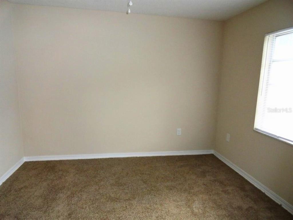 An empty bedroom features beige walls, brown carpeting, and a single window with blinds — 610 S LAKE FORMOSA DRIVE, ORLANDO, FL