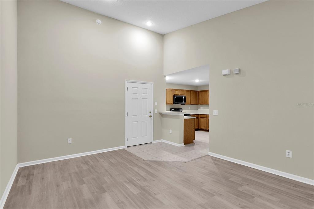 A living room with high ceilings, light-colored walls, and wood-look flooring leads to a kitchen — 6111 MAGGIES CIRCLE UNIT 110, JACKSONVILLE, FL