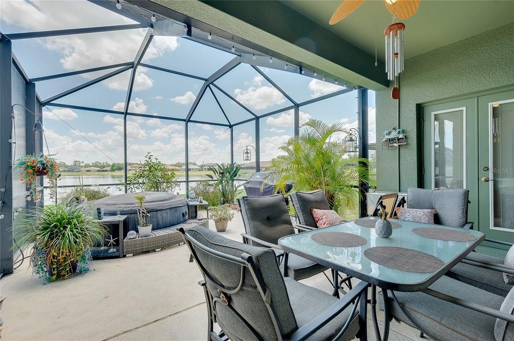 A screened-in patio features a hot tub, a covered grill, and potted plants overlooking water — 7830 113TH AVENUE E, PARRISH, FL