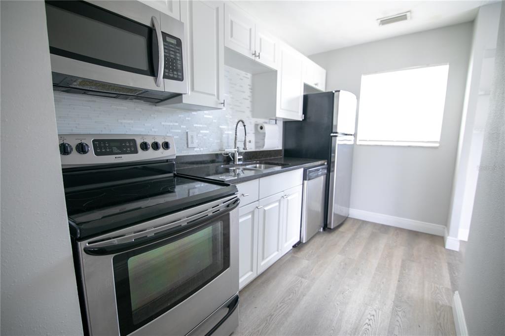 A galley kitchen features white cabinets, stainless steel appliances, and light wood-look flooring — 1831 AARON AVENUE, ORLANDO, FL