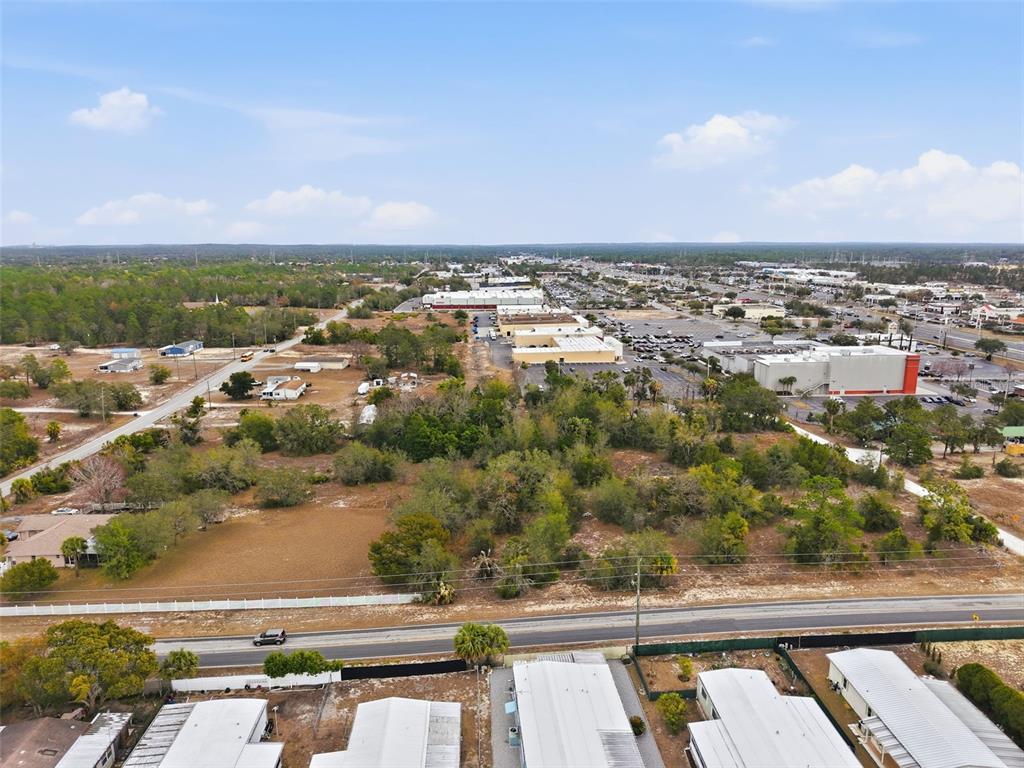An aerial view shows a vacant lot adjacent to commercial buildings and residential properties — 0 WEEPING WILLOW ROAD, BROOKSVILLE, FL