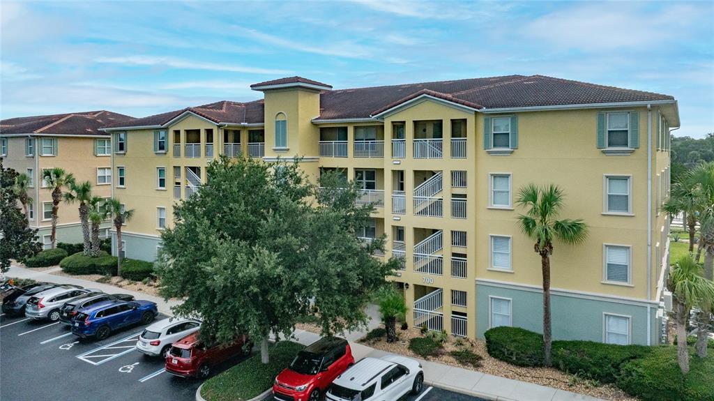 An exterior view of a multi-story yellow apartment building with a parking lot in front — 700 CANOPY WALK LANE UNIT 732, PALM COAST, FL
