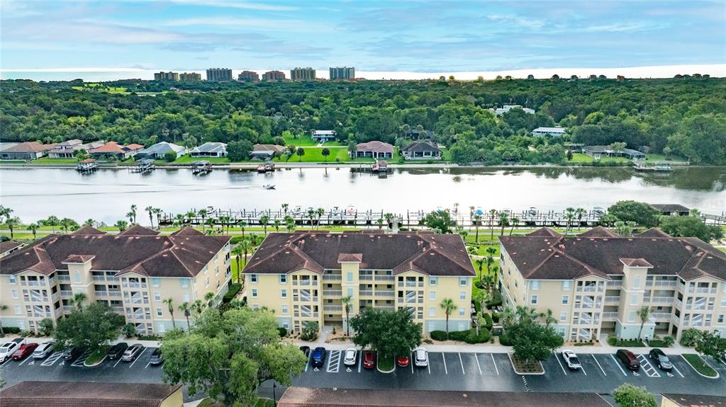 An aerial view shows three multi-story apartment buildings with parking lots beside a river — 700 CANOPY WALK LANE UNIT 732, PALM COAST, FL