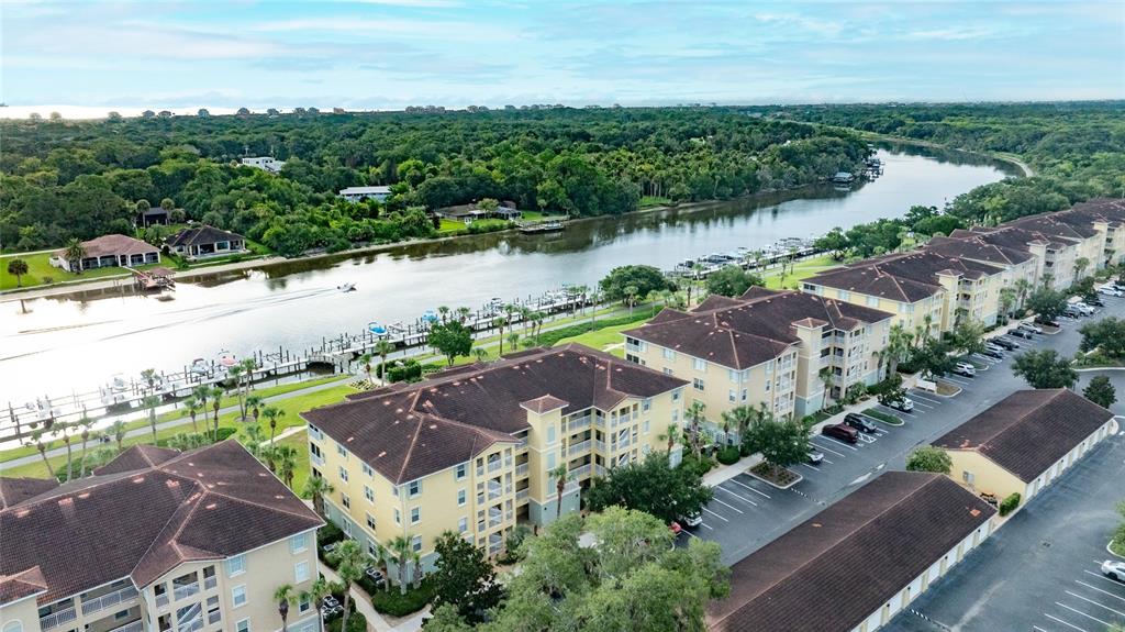 An aerial view shows multi-story apartment buildings with brown roofs situated along a river — 700 CANOPY WALK LANE UNIT 732, PALM COAST, FL