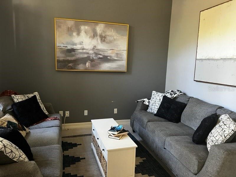 A living room features two gray sofas, a white coffee table, and abstract wall art — 845 10TH AVENUE NE, NAPLES, FL
