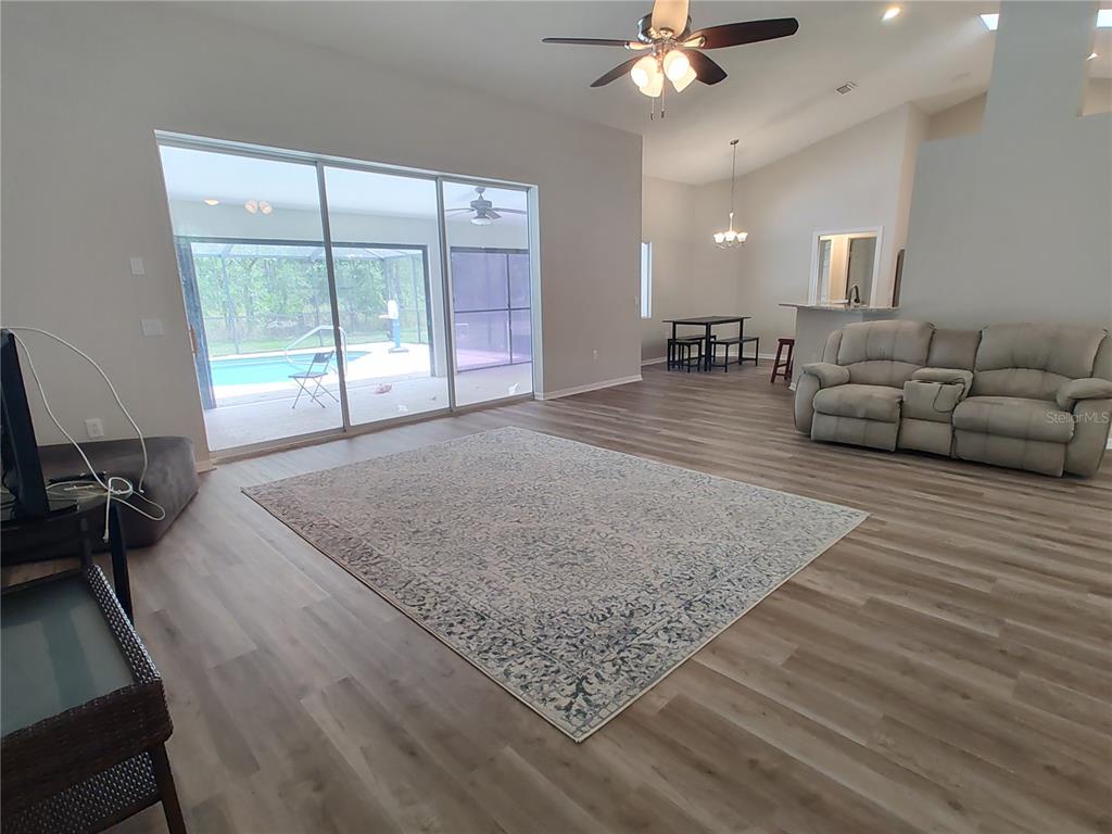 A living room with wood-look flooring, a large area rug, and sliding doors to a pool — 2905 W BEAMWOOD DRIVE, BEVERLY HILLS, FL