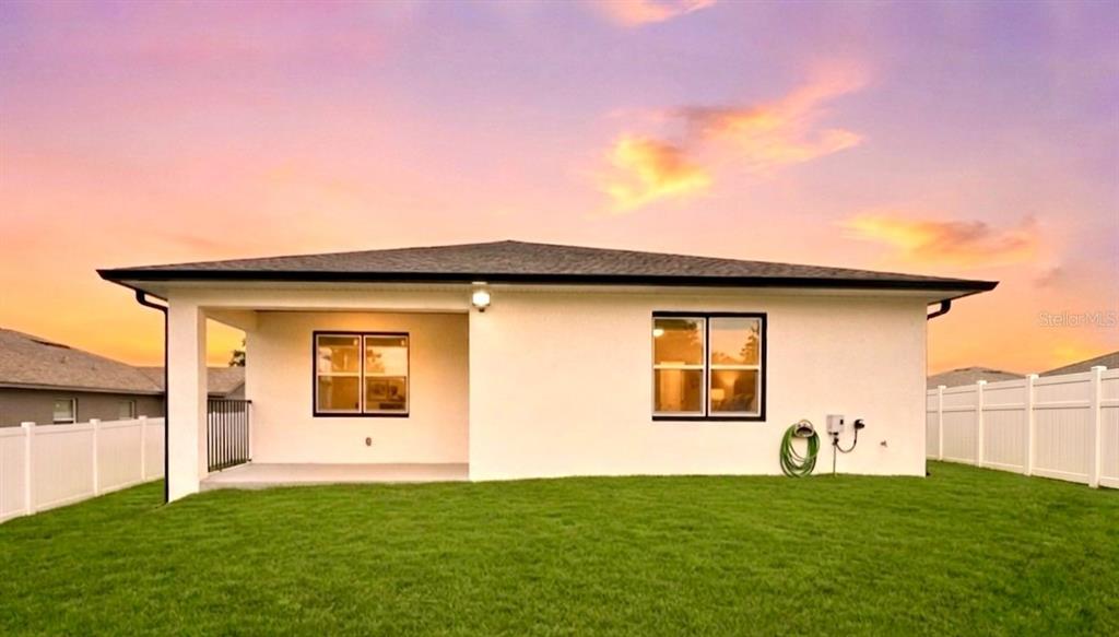 The rear exterior of a white stucco house features a covered patio and fenced yard — 105 NORTH BOULEVARD E, DAVENPORT, FL