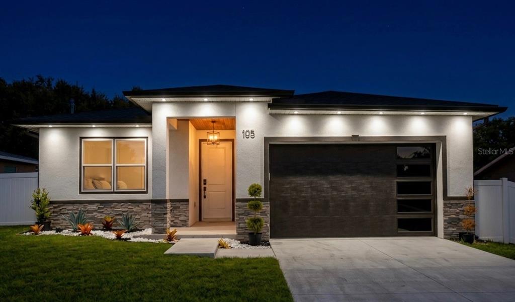 A modern single-story house with a white stucco exterior, stone accents, and a dark garage door — 105 NORTH BOULEVARD E, DAVENPORT, FL
