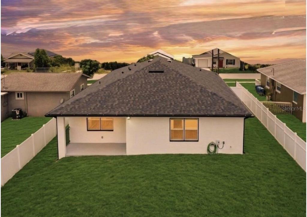 The rear exterior of a white house with a dark shingled roof and fenced yard — 105 NORTH BOULEVARD E, DAVENPORT, FL