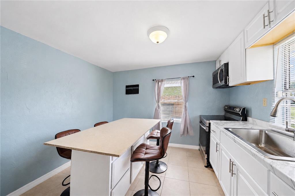 A kitchen features light blue walls, white cabinets, a central island, and brown bar stools — 516 29TH STREET E, PALMETTO, FL